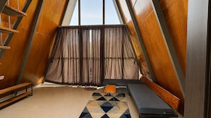 Una habitación triangular con un banco, una mesita y un tapete estampado.