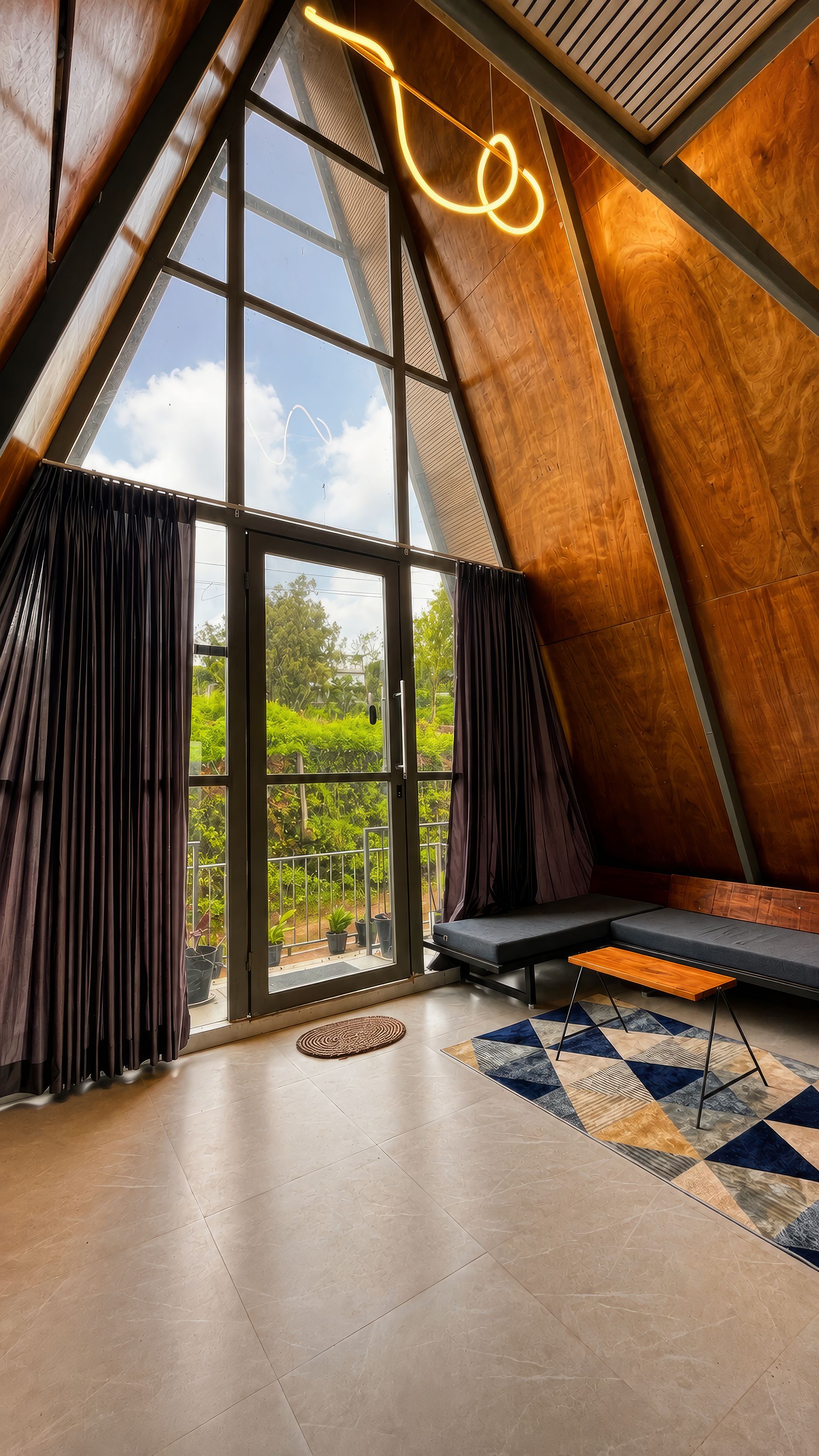 Un interior moderno con techo inclinado, ventanas grandes, un sofá y una alfombra estampada.