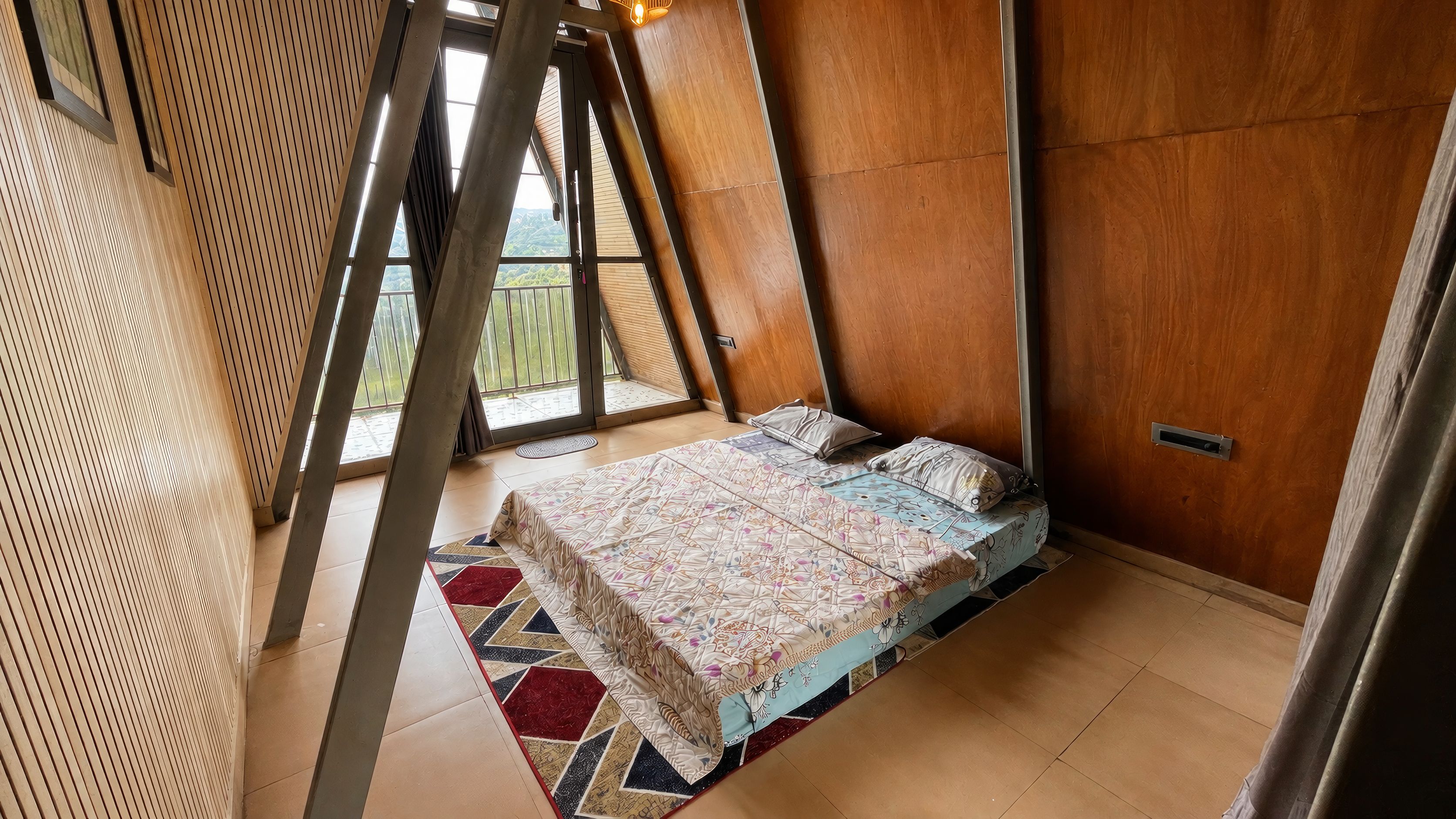 Ein Zimmer mit schrägem Dach, einem Bett mit gemusterten Textilien und Blick ins Grüne.