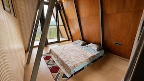 Una habitación con techo inclinado, una cama con ropa de cama estampada y vistas al exterior con vegetación.