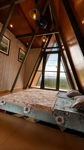 Un dormitorio con techo inclinado, cama con ropa de cama floral, lámpara colgante y ventana con vistas al exterior.