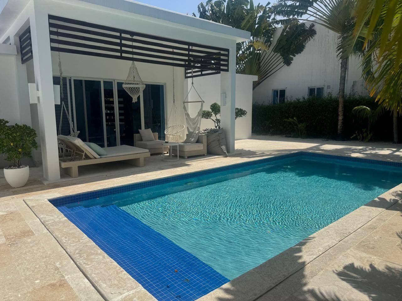 A modern pool area with a clear blue pool, lounge chairs, and a covered seating area.