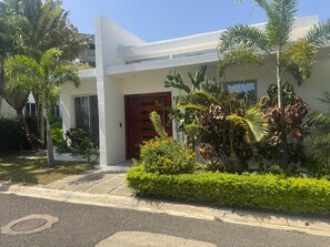 A modern building with a red door, surrounded by well-maintained greenery and palm trees. - Sosua Ocean Village - Las Palmas Villa #4 (Sosúa)