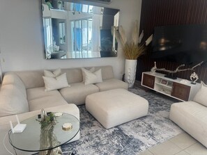 Ein modernes Wohnzimmer mit einer Couch, einem Hocker und einem Glastisch.