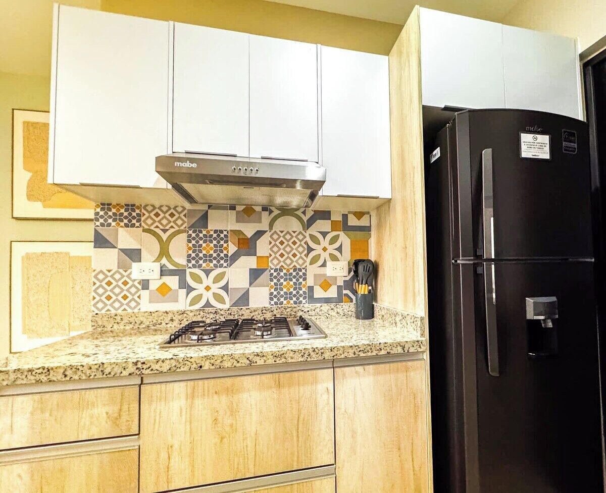 A kitchen with a gas stove, a black refrigerator, and patterned backsplash tiles.