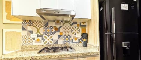 A kitchen with a gas stove, a black refrigerator, and patterned backsplash tiles.