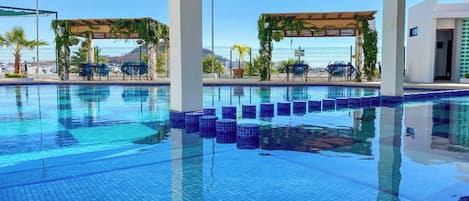 A swimming pool with clear blue water, surrounded by lounge chairs and covered seating areas.