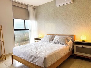 Ein Schlafzimmer mit einem Bett, zwei Nachttischen, einem Fenster mit Blick und einer Klimaanlage.