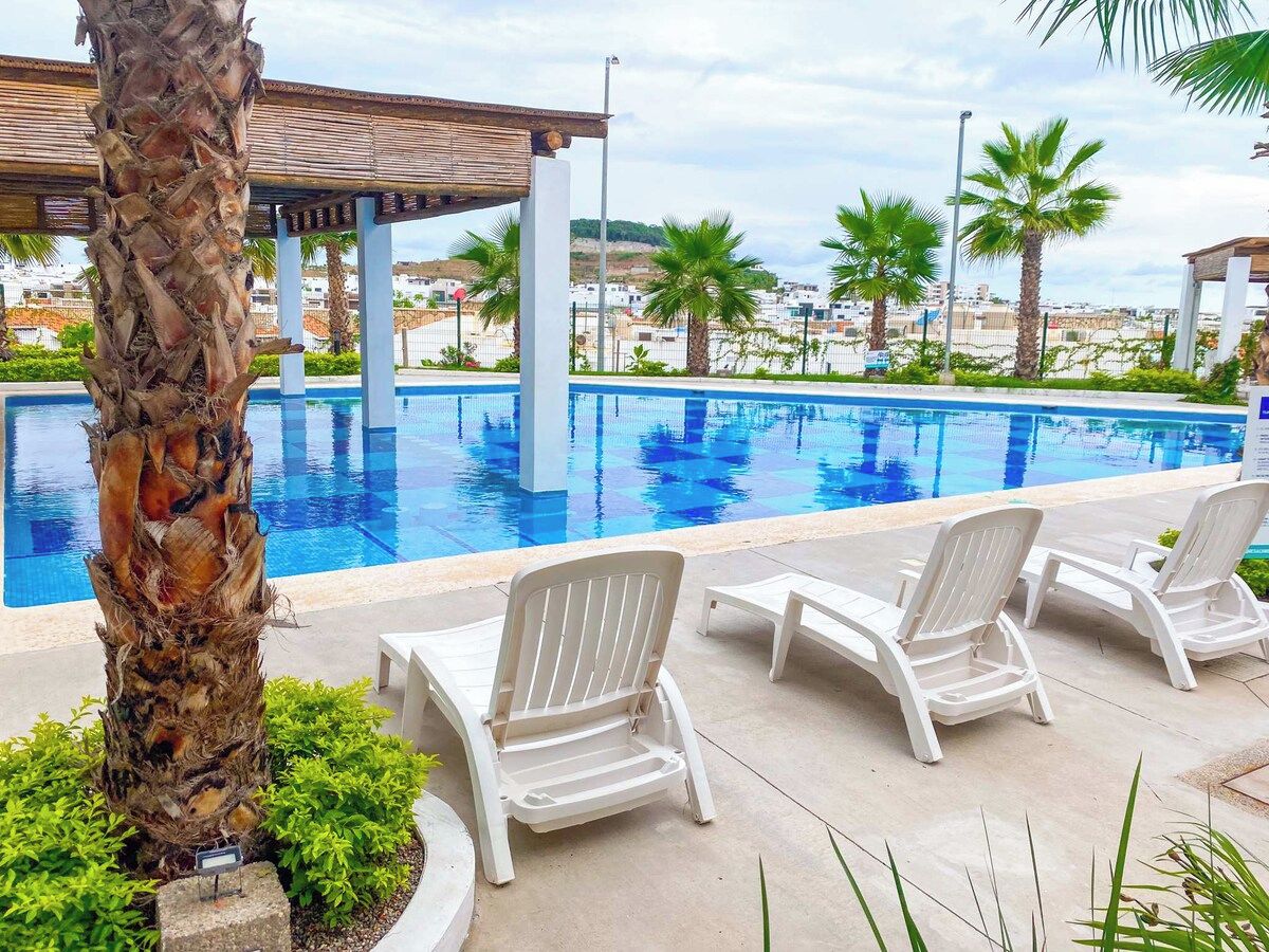 A poolside area with lounge chairs, a palm tree, and a view of the surrounding landscape.