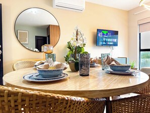 A dining area with a round table, wicker chairs, a television mounted on the wall, and a potted plant. - Indigo, Modern Apt Steps from Playa Brujas Beach (Mazatlán)