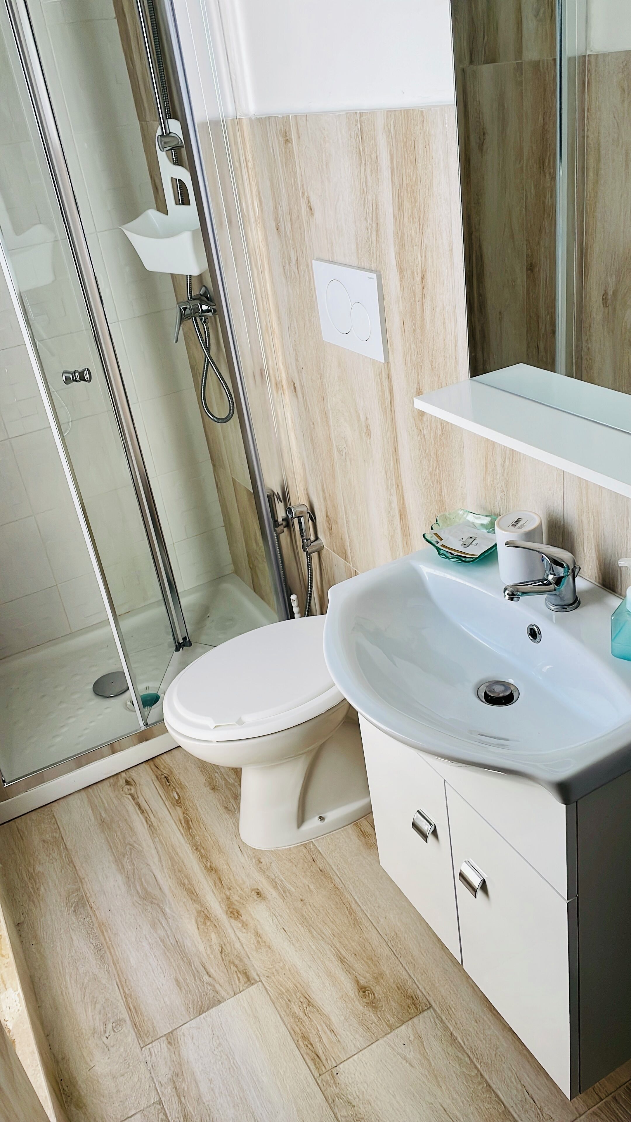 Een moderne badkamer met een glazen douchecabine, een wit toilet en een wastafel met spiegel.