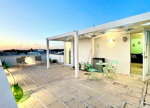 Eine Dachterrasse mit überdachter Sitzgelegenheit, einem Tisch und Stühlen.