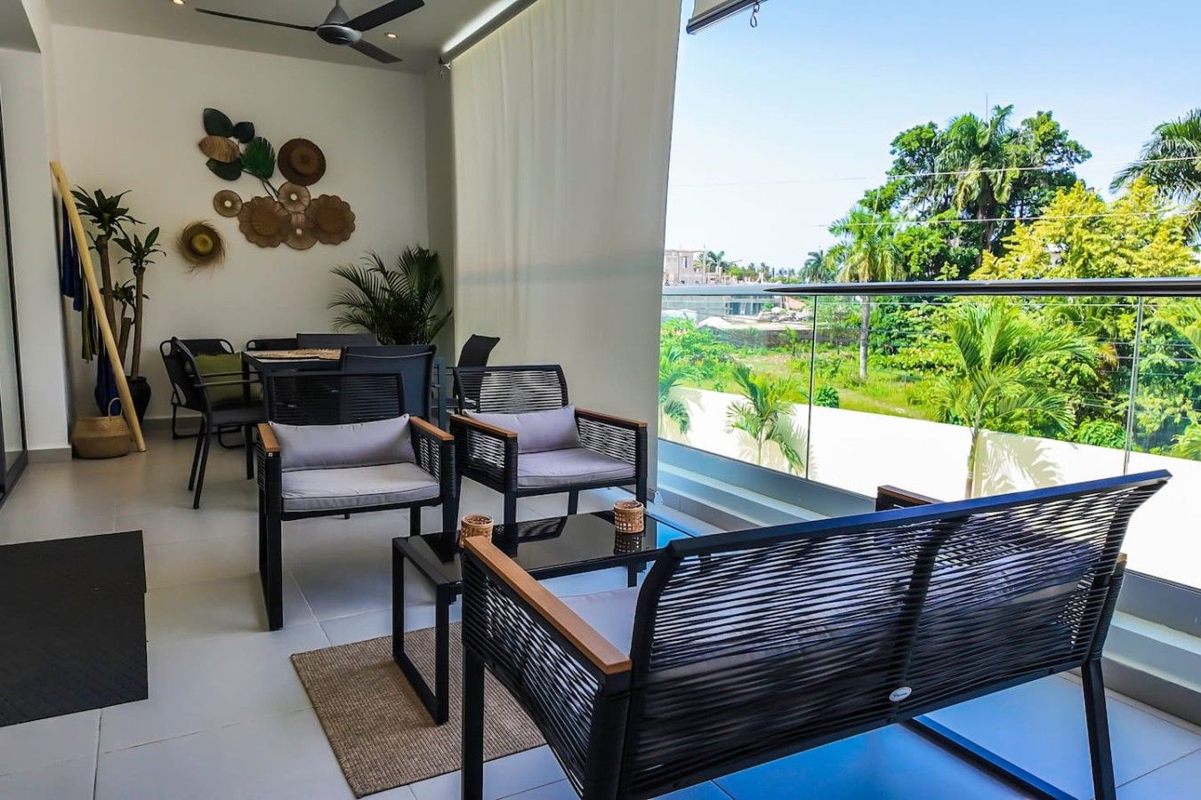 A modern living room with a balcony, furnished with black chairs and a dining table, and decorated with wall art and plants.