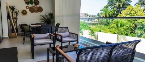 A modern living room with a balcony, furnished with black chairs and a dining table, and decorated with wall art and plants.