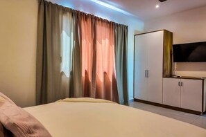 A hotel room with a bed, a wardrobe, a television, and curtains. - Poolside 2 Bedroom Apartment (Las Terrenas)