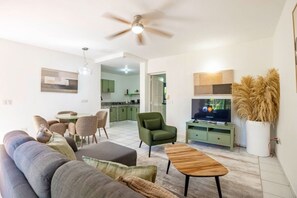 A living room with a sofa, chairs, a coffee table, a television, and a ceiling fan. - One Bedroom Central Apartment (Sosúa)