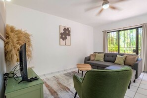 Un salon avec un canapé, un téléviseur, une petite table et une chaise.