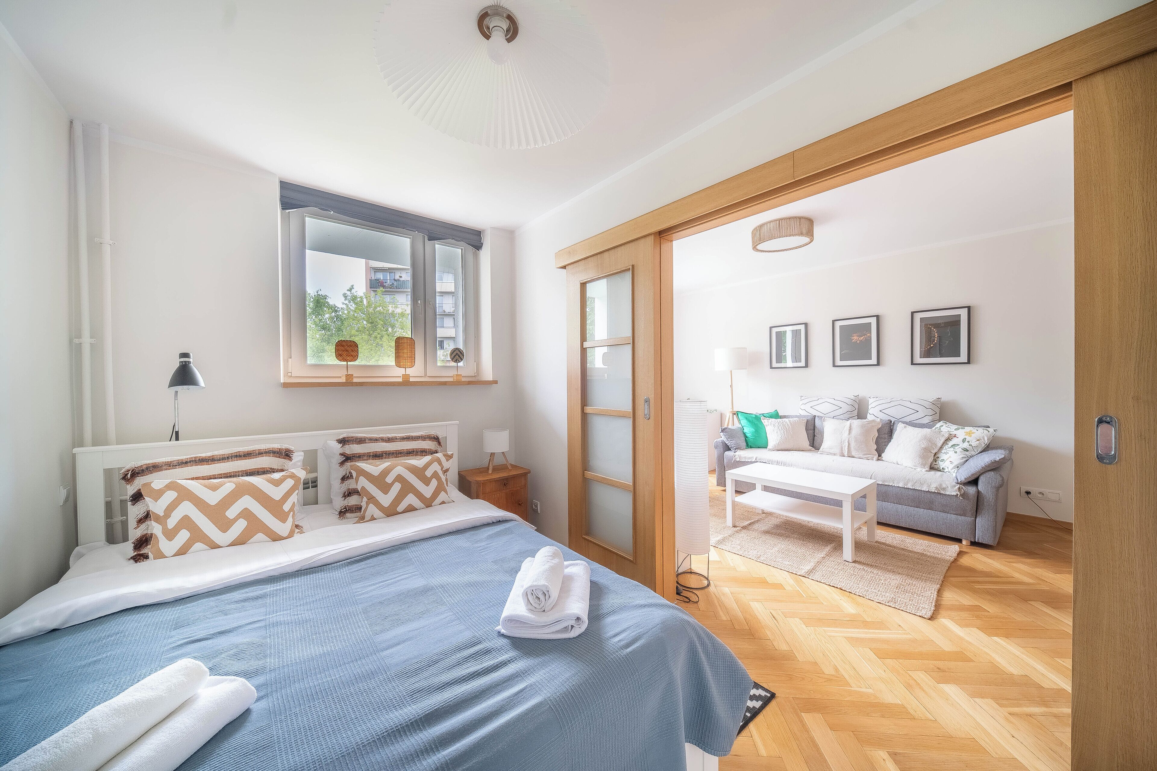 A bedroom with a bed, bedside table, and a view of a living area with a sofa and a coffee table.