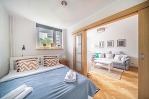 Une chambre à coucher comprenant un lit, une table de chevet et donnant sur un espace de vie avec un canapé et une table basse.