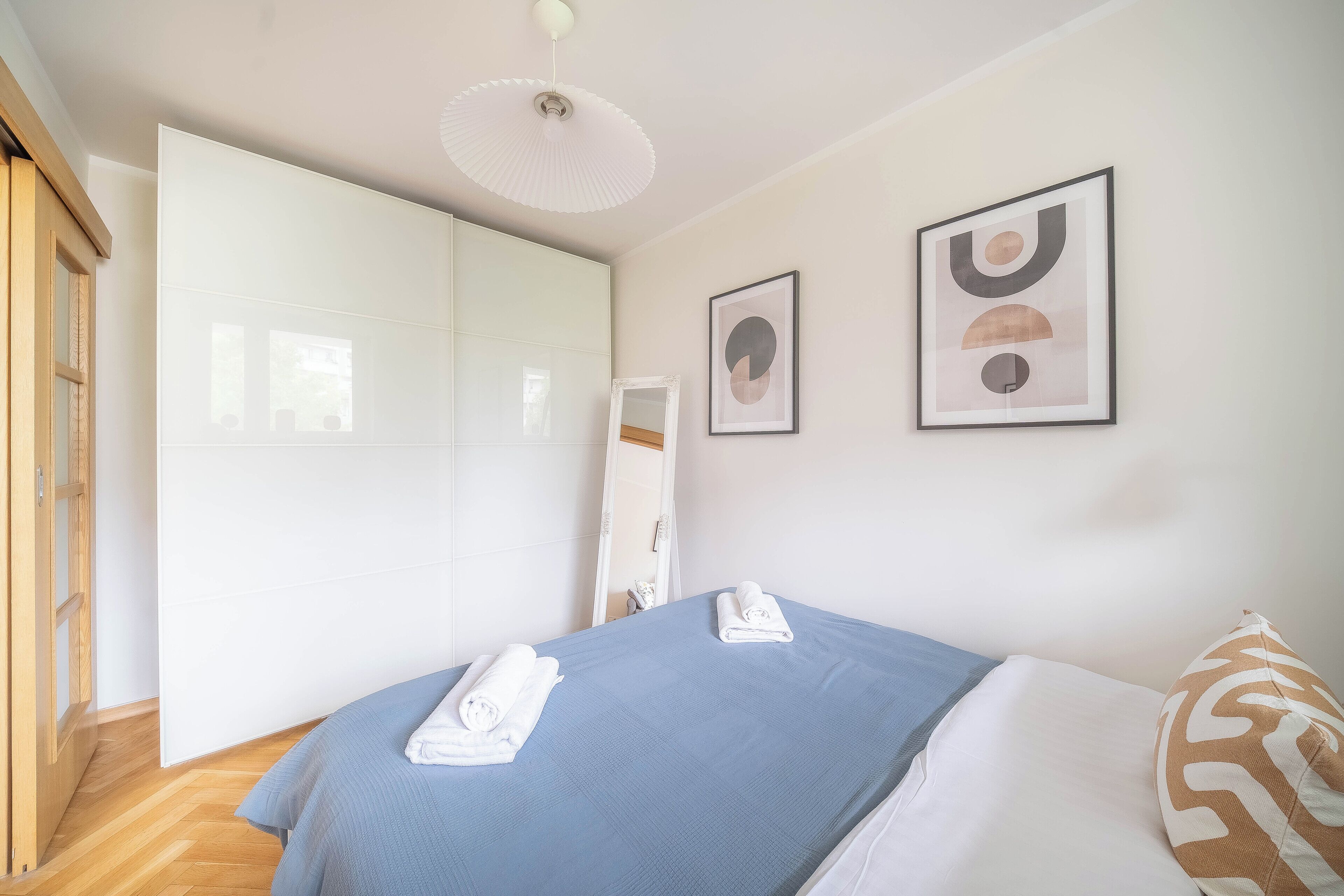 A bedroom with a bed, a wardrobe, and two framed artworks on the wall.