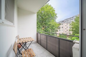 A balcony with a wooden bench and a view of a tree and buildings.