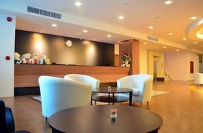 A hotel lobby with a reception desk, white armchairs, a round table, and a clock on the wall. - Tevan Jomtien Hotel (Pattaya)