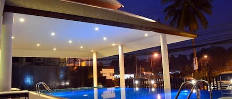 An indoor swimming pool with a covered area, seating, and a palm tree in the background.