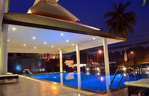 An indoor swimming pool with a covered area, seating, and a palm tree in the background.
