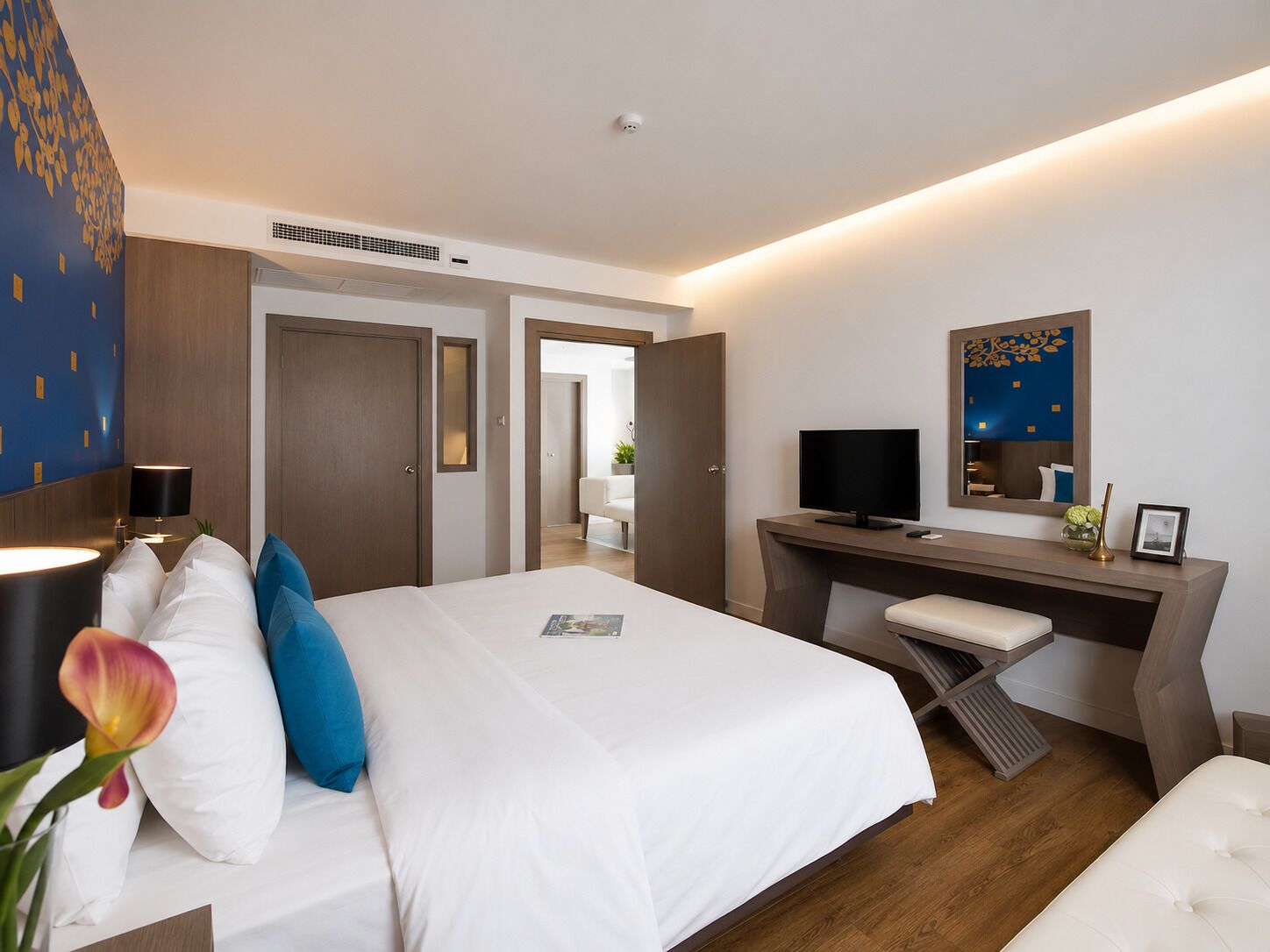 Habitación de hotel con cama, escritorio, televisor y espejo.