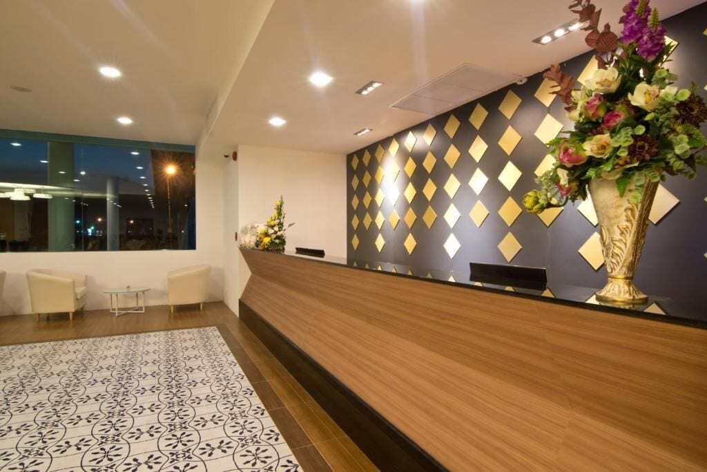 Ein Hotel-Rezeptionsbereich mit modernem Design, der einen Empfangstresen, ein gemustertes Parkett und eine Wand mit geometrischen Mustern zeigt.