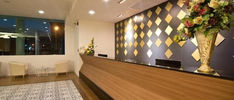 A hotel reception area with a modern design, featuring a reception desk, a patterned floor, and a decorative wall with geometric patterns.