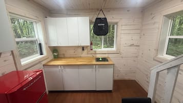 Et lille køkken med trævægge, hvide skabe, en rød hårdelem og en hængende taske.