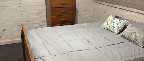 Un dormitorio con techo inclinado, estructura de cama de madera, una mesita de noche y una ventana.