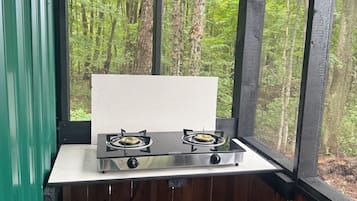 Une petite cuisine équipée d’une cuisinière à gaz et d’une bouteille de propane, donnant sur une forêt.