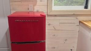 A red refrigerator with a digital display, a window with a view of trees, and a wooden wall.
