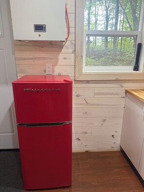 Un réfrigérateur rouge doté d’un écran numérique, une fenêtre donnant sur des arbres et un mur en bois.