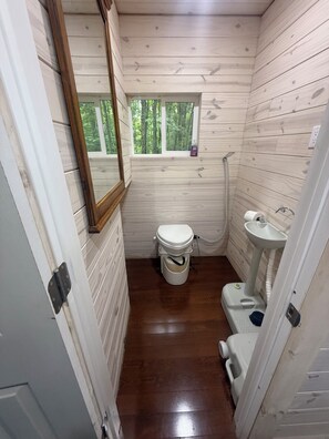 A compact bathroom with a wooden interior, a window, a toilet, and a sink. - Off the beaten path… (Algonquin Highlands)