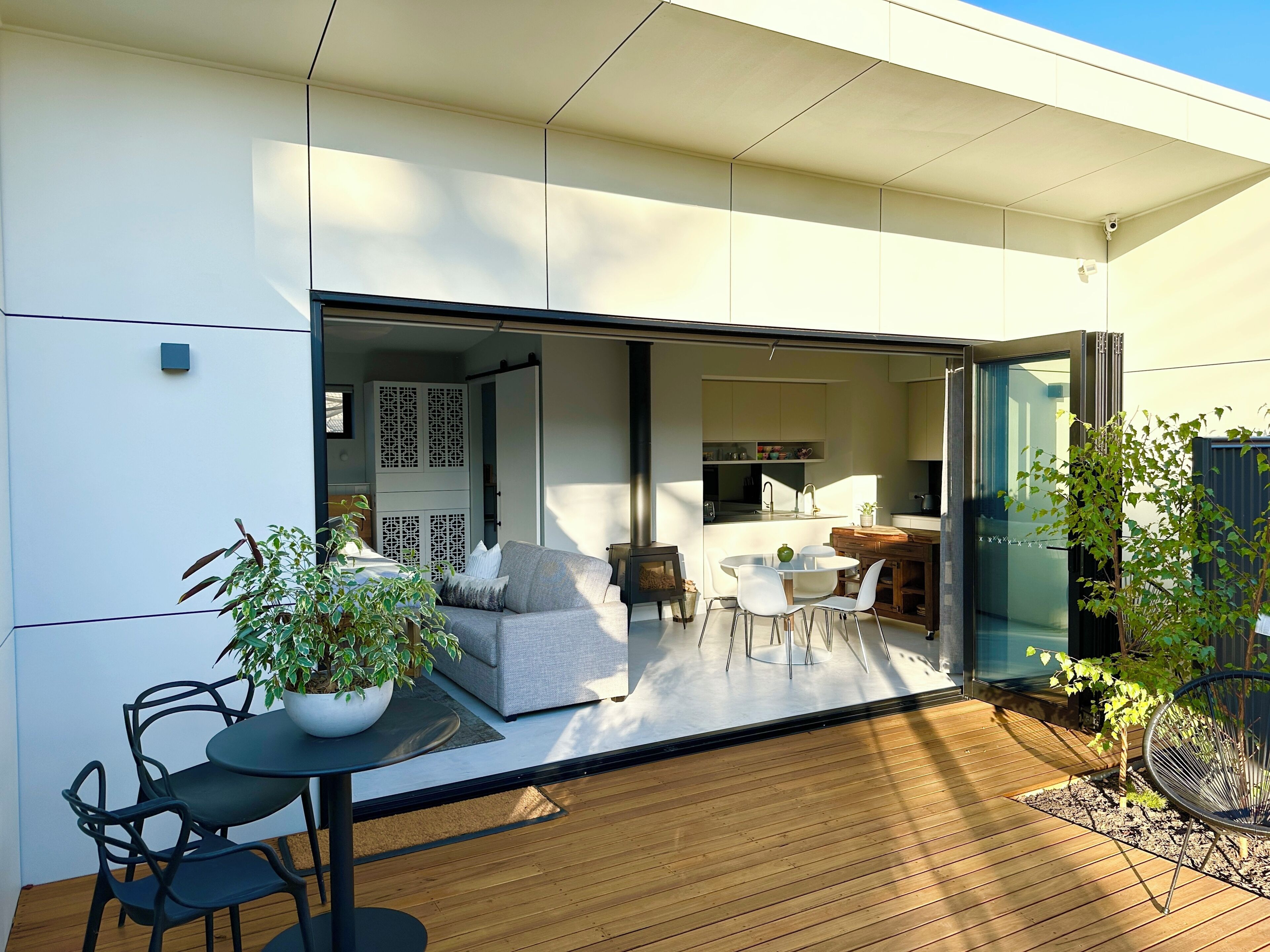A modern house with a patio area featuring a dining table, chairs, and potted plants.