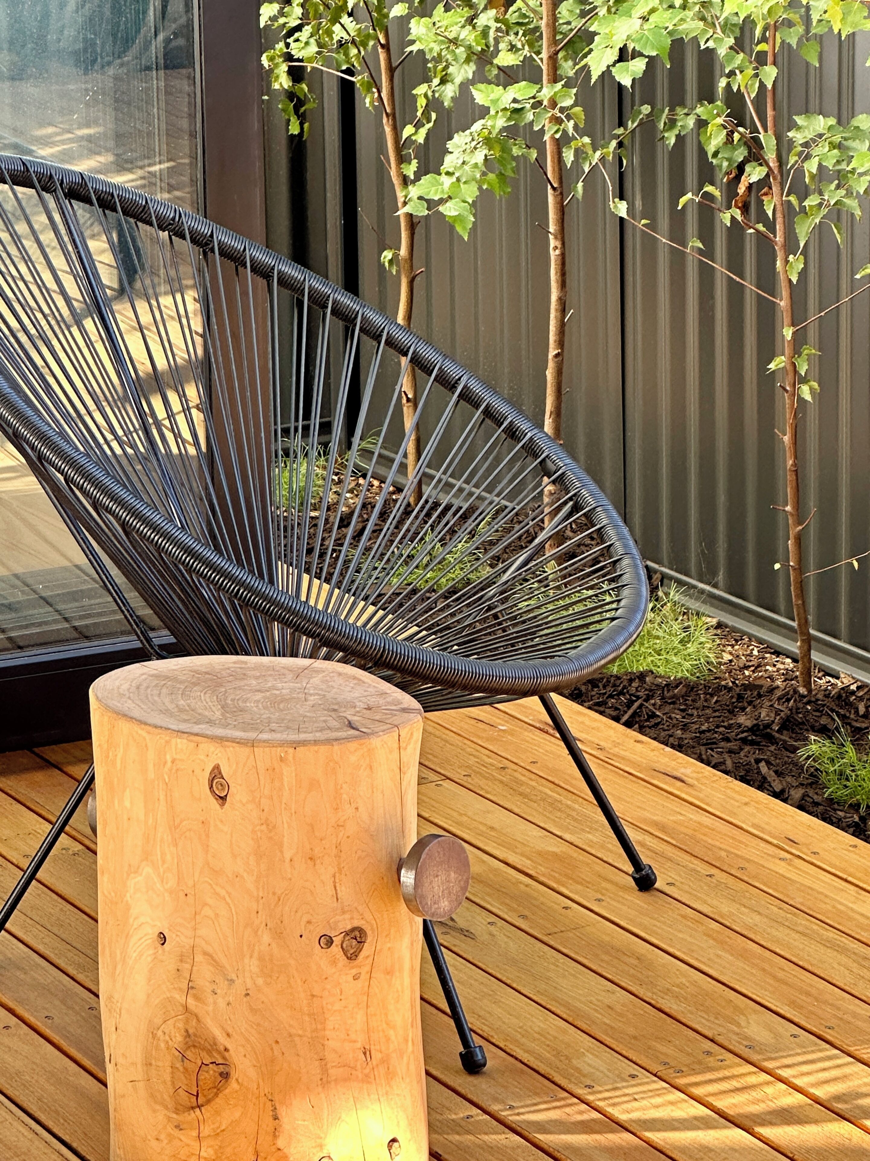 Une chaise en fil de fer noir avec un tabouret en bois servant de base, le tout posé sur une terrasse en bois.