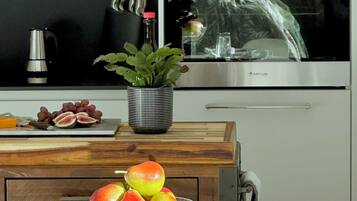 A modern kitchen with stainless steel appliances, a fruit bowl on the counter, and a dining area set with placemats and cutlery.