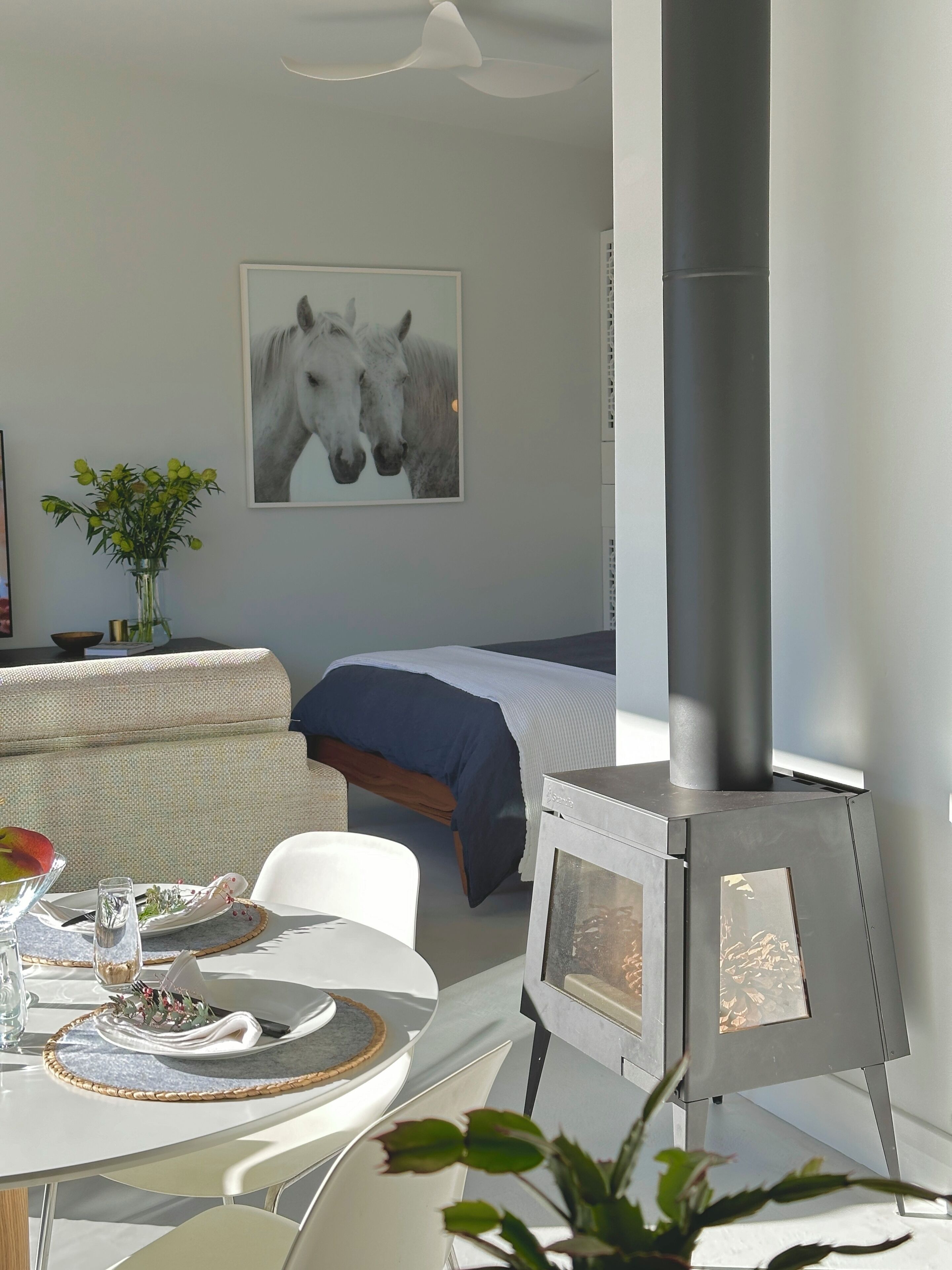 A modern room with a bed, a dining table set for two, a fireplace, and a horse-themed artwork on the wall.