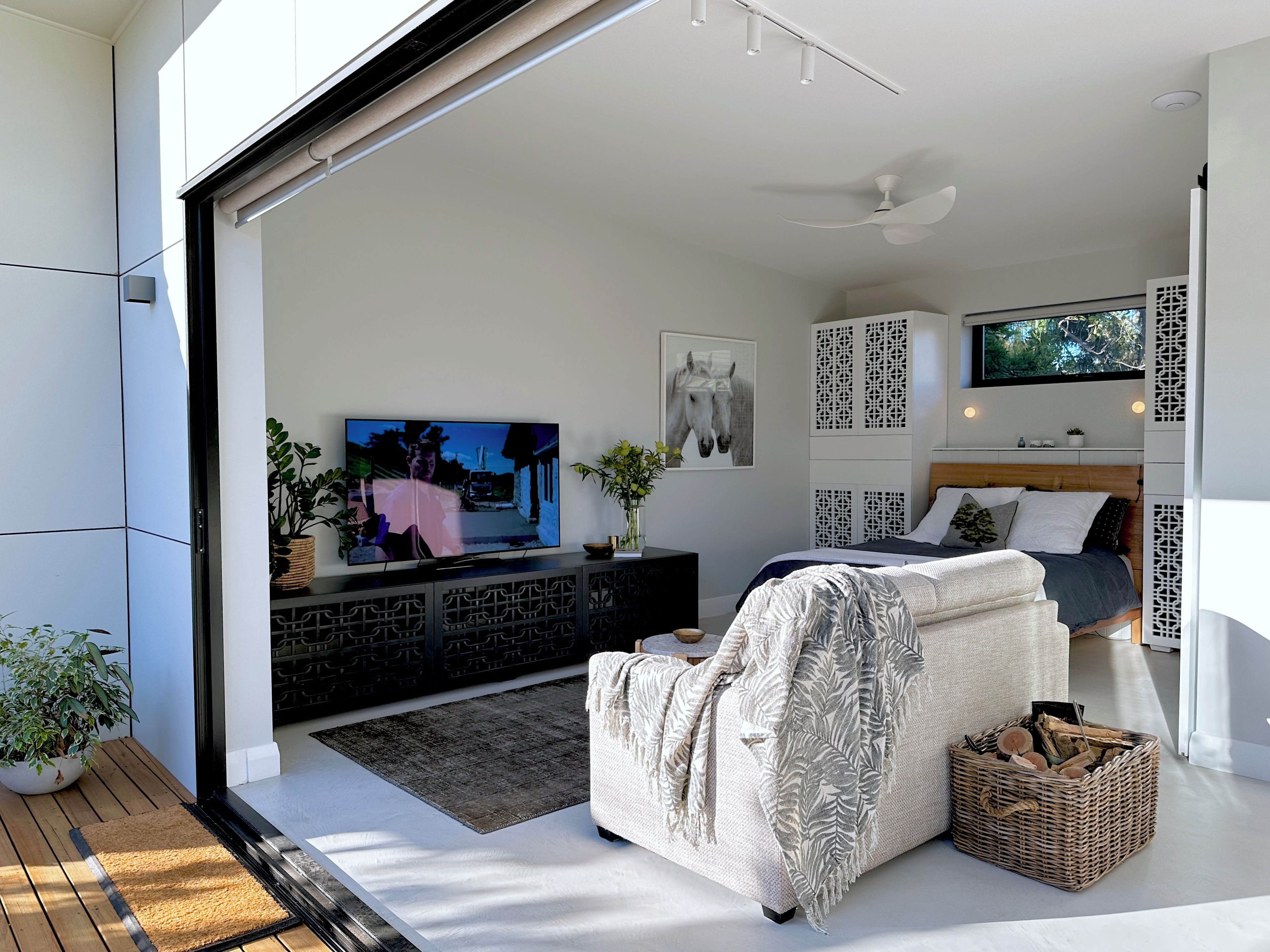 A modern bedroom with a large flat-screen TV, a bed with a headboard, a sofa, and a decorative wall panel.