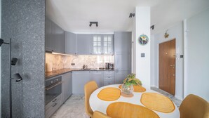A modern kitchen with grey cabinets, a marble countertop, and a dining area with a white table and yellow chairs. - Yellow Vibe Złota (Warszawa)
