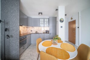 A modern kitchen with grey cabinets, a marble countertop, and a dining area with a white table and yellow chairs. - Yellow Vibe Złota (Warszawa)