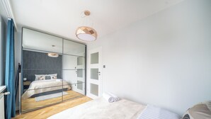 A modern bedroom with a large mirror, a bed with a white duvet, and a hanging light fixture. - Yellow Vibe Złota (Warszawa)