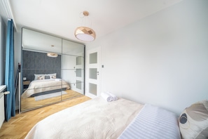 A modern bedroom with a large mirror, a bed with a white duvet, and a hanging light fixture. - Yellow Vibe Złota (Warszawa)