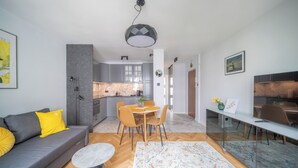 A modern living room with a grey sofa, a dining area with a round table, and a kitchen in the background. - Yellow Vibe Złota (Warszawa)