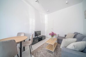 Ett modernt vardagsrum med en soffa, ett soffbord, en tv och en matplats med stolar.