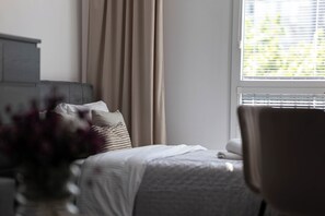 A bedroom with a bed, a chair, a window with blinds, and a curtain. - Grzybowska City Center, Wola,Warsaw (Wola)