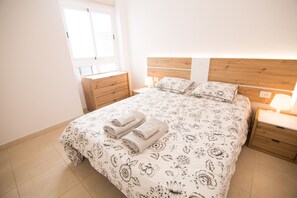 Ein Schlafzimmer mit einem Holz-Kopfende, einem Bett mit floralem Bettzeug, zwei Nachttischen mit Lampen und einem Fenster mit Jalousien.